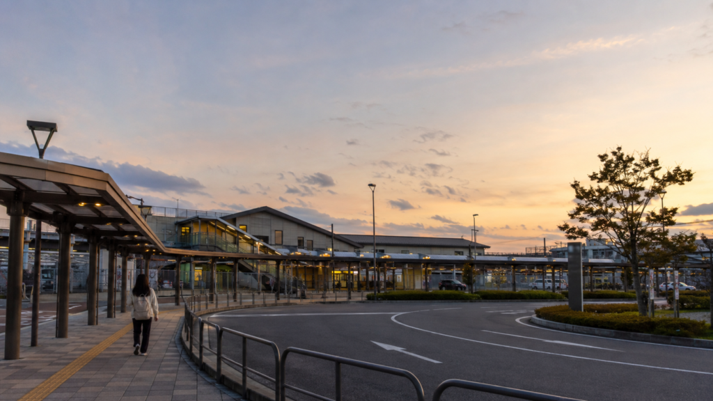 夕方の駅前ロータリーと歩道を歩く人の後ろ姿