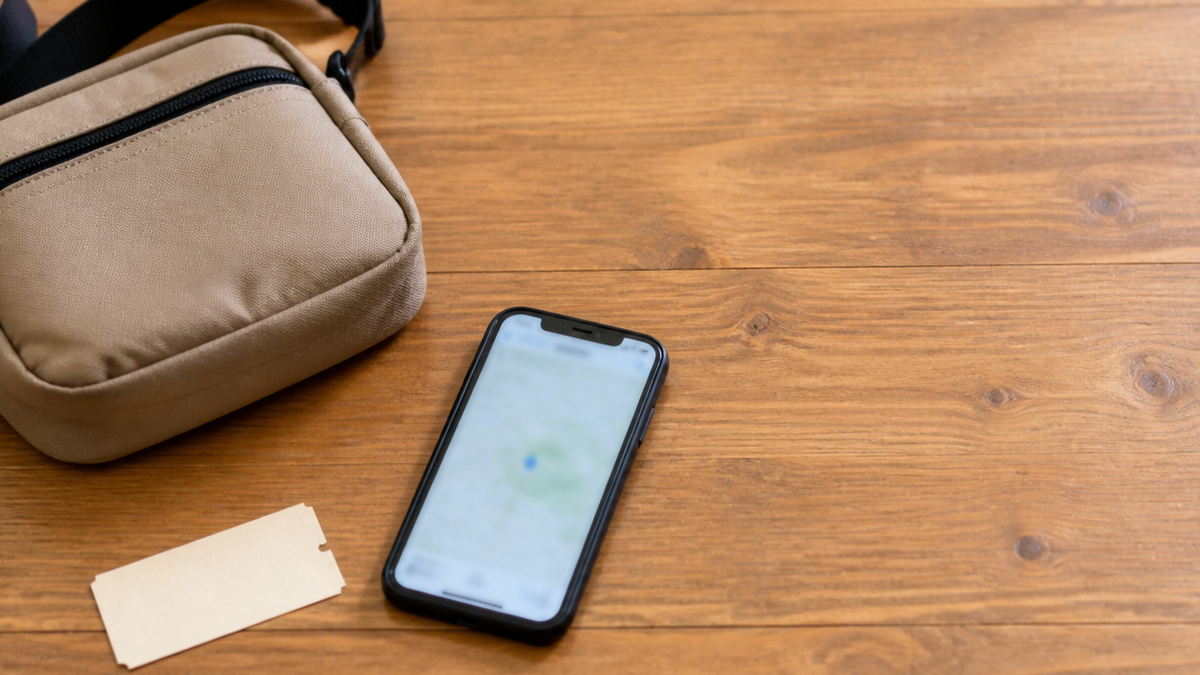 小さめのショルダーバッグと乗換案内アプリを開いたスマートフォン、無地の切符が置かれたテーブル