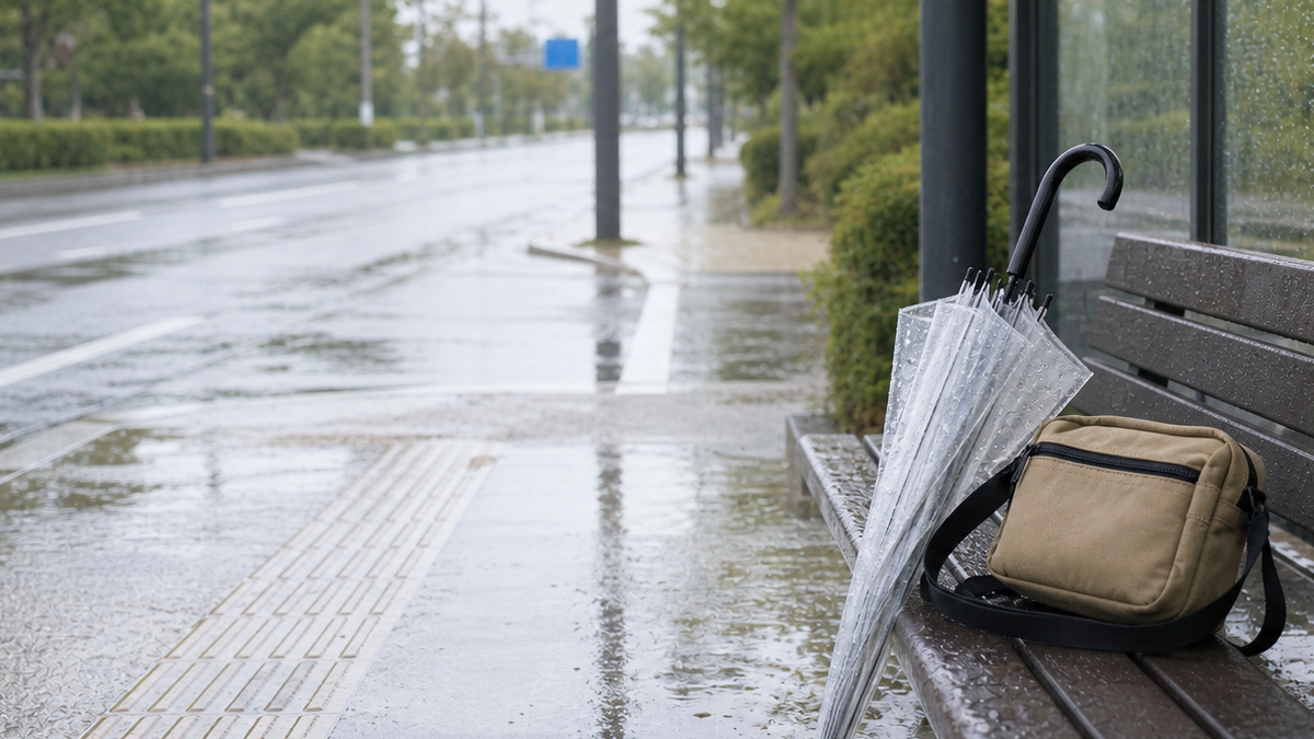 雨の日のバス停に置かれた傘とショルダーバッグ