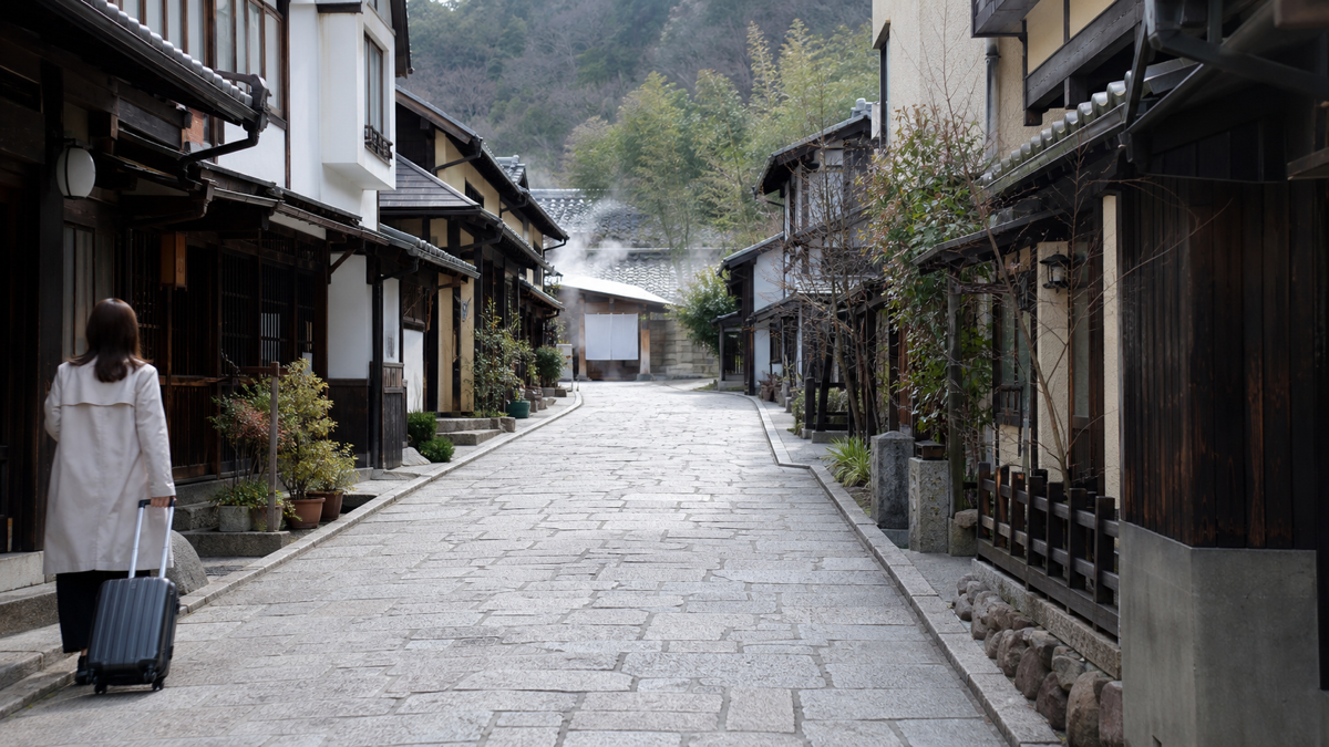 旅行バッグを持って緩やかな道を歩く温泉街散策のイメージ