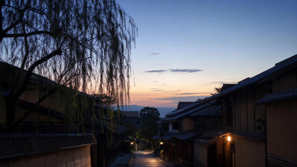 夕暮れの温泉街に柳並木と外湯の明かりがともる様子