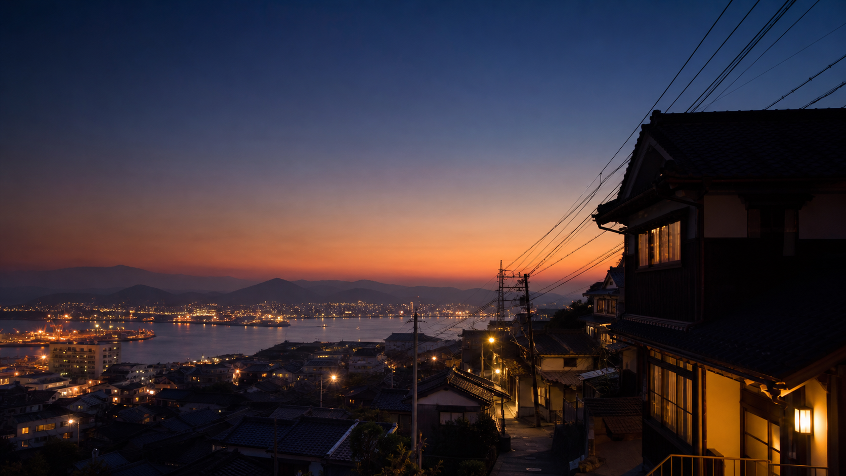 坂道沿いの家並みと、その先に広がる港町の夜景