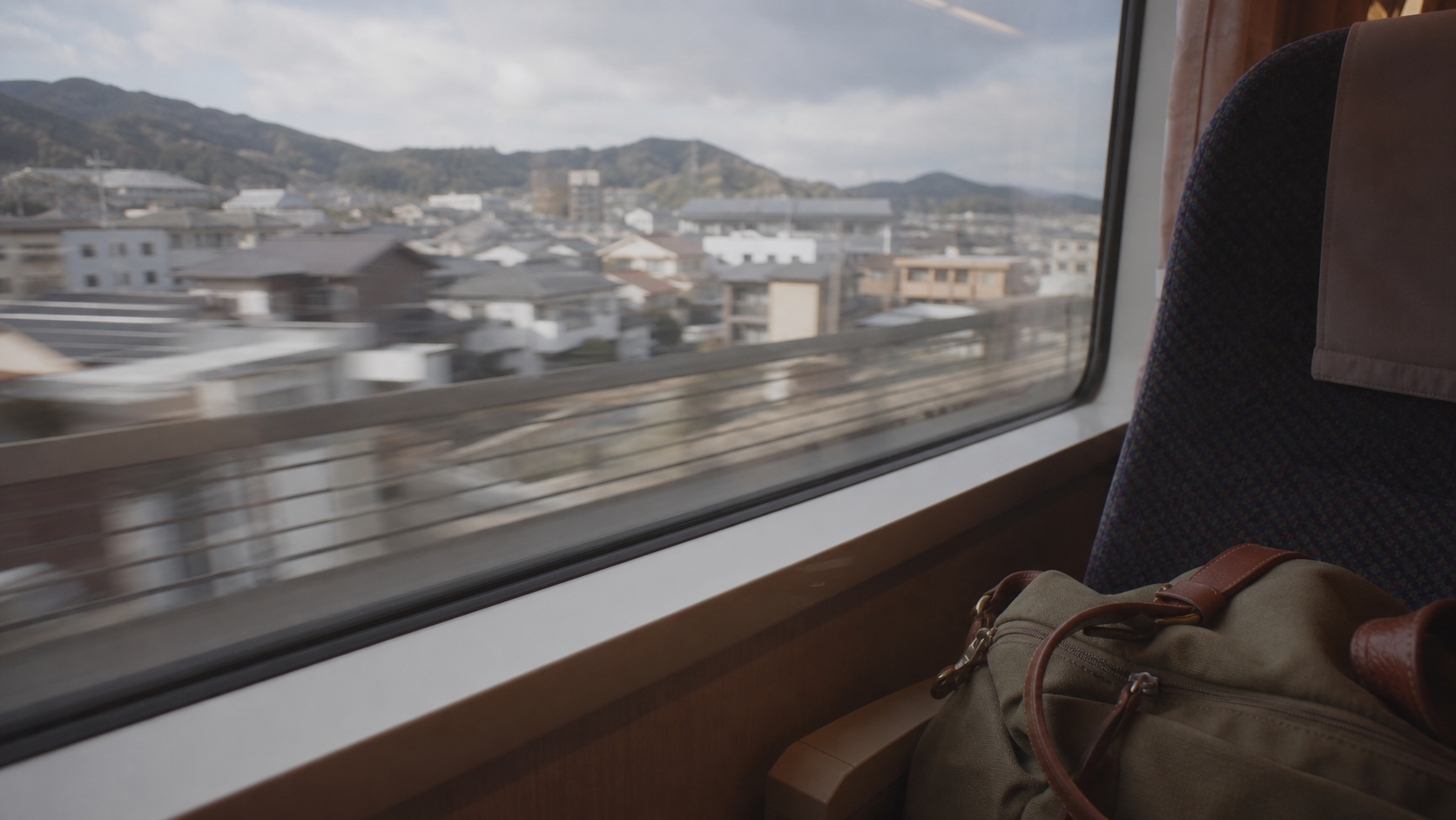 車窓を流れる街並みと隣の座席に置かれた旅行バッグ